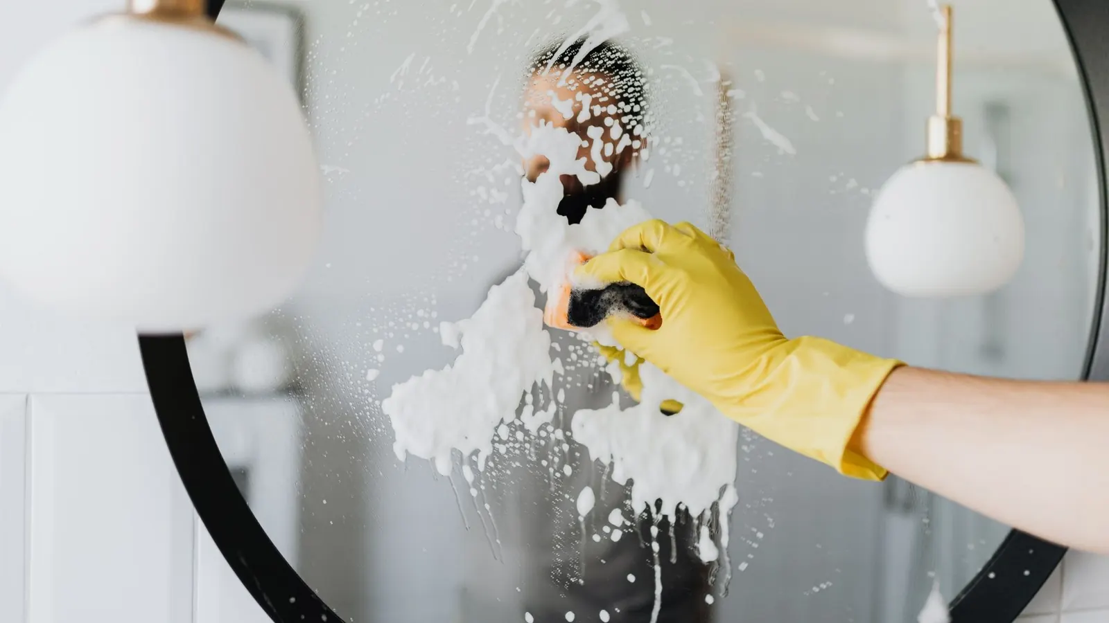 Yellow-glove hand scrubbing a bathroom mirror during residential cleaning service in Palm Springs CA